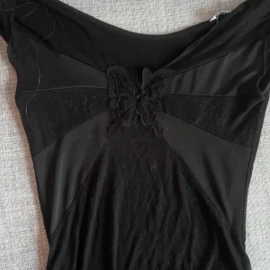 Svart topp med fjärilsdetalj Eve XS - Supersnygg svart topp från Eve i storlek XS. Toppen har en unik fjärilsapplikation framtill och är sydd i paneler som ger coola linjer. Perfekt för dig som gillar detaljer som sticker ut och vill ha en topp med edge.