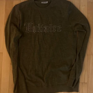 Olivgrön stickad tröja Zadig & Voltaire - Snygg olivgrön stickad tröja från Zadig & Voltaire med coolt Voltaire-tryck i glittriga stenar på bröstet i 100% merinoull. Nypris på denna är kring 2500 kr. Tröjan har rund hals och långa ärmar, perfekt för lager-på-lager och chill vibes.