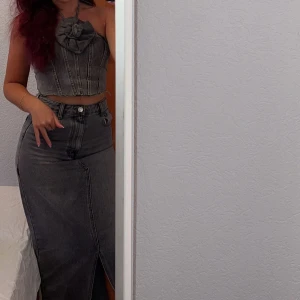 Grå lång jeanskjol med slits - Säljer en snygg grå långkjol i jeans med hög midja och en stilren slits framtill. Kjolen har klassiska jeansdetaljer som fickor och bälteshällor. Perfekt för dig som gillar en edgy och trendig look. (Topp med ros följer med)