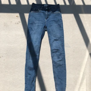 Blå skinny jeans med hög midja - Snygga blå skinny jeans från 157 med hög midja och klassisk femficksdesign. Jeansen har smal passform, dragkedja och knapp framtill samt bälteshällor. Perfekta för dig som gillar en tight och stilren look.