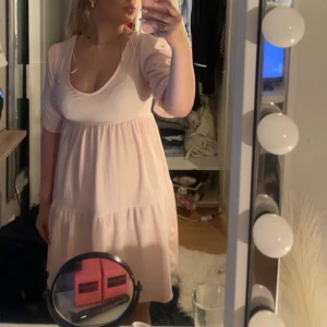 Ljusrosa kortklänning med puffärm - Supersöt ljusrosa klänning med djup v-ringning och puffiga trekvartsärmar. Klänningen har en flowy passform och är tillverkad i ett lätt, krinklat tyg som känns luftigt. Perfekt för sommarens varma dagar och ger en romantisk vibe.