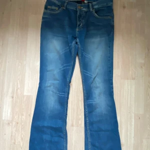 Blå bootcut jeans med slitningar - Säljer ett par blå jeans med bootcut-modell och snygga slitningar framtill. Klassisk femficksdesign och normal passform. Jeansen har en cool tvättad look och är perfekta för dig som gillar en avslappnad stil.