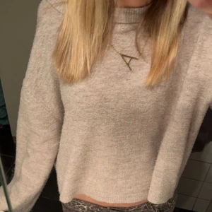 Beige stickad tröja med rund hals - Mysig beige stickad tröja med rund halsringning och lång ärm. Tröjan har en enkel och stilren design, perfekt att matcha med jeans eller kjol. Den är lite croppad och har en mjuk känsla som gör den superbekväm.