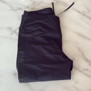 Svarta leggings från ICANIWILL - Svarta leggings från ICANIWILL med hög midja och snörning i midjan. Snygga detaljer med logga längs sidorna och reflekterande mönster på benet. Tillverkade i stretchigt syntetmaterial som passar perfekt för träning.