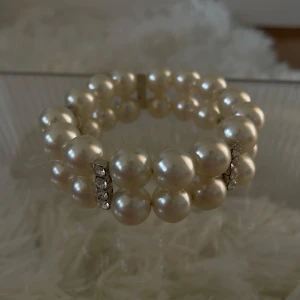 Pärlarmband  - Stilrent armband med två rader stora vita pärlor och glittrande strassdetaljer i silver mellan pärlorna. 