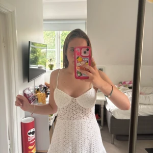 Zara klänning - Supersöt vit kort klänning med tunna axelband och volang nertill. Klänningen har broderat hålmönster och lätt v-ringad byst. Perfekt för varma dagar och har en luftig passform som känns riktigt fräsch.