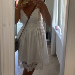 ZARA klänning  - Superfin vit kortklänning med smala axelband, v-ringad spets upptill och broderade detaljer. Klänningen har smockad midja och volangkant med spets nertill. Perfekt för sommarens alla tillfällen, riktigt söt och luftig modell. Använd fåtal gånger, så fint skick. Pris går att diskutera! 