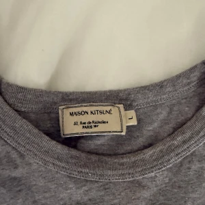 Grå t-shirt Maison Kitsuné rävpatch - Tjena säljer ni en Grå t-shirt från Maison Kitsuné med klassisk rund hals och liten broderad rävpatch på bröstet. T-shirten är i mjuk bomull och har en enkel, clean look som passar perfekt till jeans eller shorts. Använd ungefär 4 gånger legat i min garderob i 3 år ungefär… 