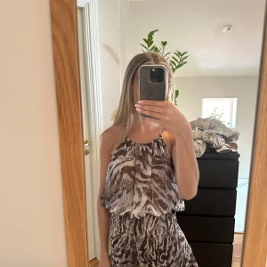 Zebra mönstrad klänning från Zara slutsåld  - Supersöt kortklänning från Zara i brunvitt zebra  mönster med tunna axelband och volangdetaljer nertill. Klänningen har knytning i nacken och är ärmlös med luftig passform. Perfekt för varma dagar när du vill sticka ut lite extra. Slutsåld och eftertraktad, i super skick, storlek xs