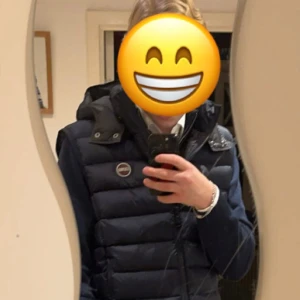 Mörkblå dunväst från Colmar - Säljer en mörkblå dunväst från Colmar med avtagbar huva och diskret logga på bröstet. Västen har en quiltad design och stängs med dragkedja. Perfekt för lager-på-lager och snygg till både hoodie och skjorta. Använd ett fåtal gånger, köptes i december 2024!!