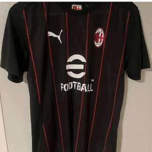 AC Milan matchtröja - AC Milan fotbollströja från Puma med svarta och röda vertikala ränder. Tröjan har klubbmärke på bröstet, vit Puma-logga och sponsortryck. Tillverkad i tekniskt Drycell-material som andas. Perfekt för dig som vill visa ditt stöd för Milan.