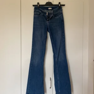 Blå bootcut jeans från Nelly - Snygga blå bootcut jeans från Nelly med klassisk femficksdesign och broderade bakfickor. Jeansen har normal passform och är tillverkade i ett mjukt denimtyg som sitter skönt hela dagen. Perfekta för dig som gillar en retroinspirerad look.