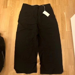 Svarta byxor från Carin Wester - Svarta byxor från Carin Wester i modellen Betsy. Vida ben och hög midja ger en chill och trendig look. Byxorna är tillverkade i en mix av linne och viskos, vilket gör dem både svala och snygga. Perfekta för dig som gillar stilrena och bekväma plagg. Storlek 40