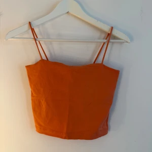 Orange/aprikos  croppad linnetopp Gina Tricot - Snygg orange/aprikos croppad linnetopp från Gina Tricot med tunna axelband. Enkel och stilren design i mjuk bomull, perfekt till sommaren. Toppen har en tight passform och är ärmlös för en fräsch look. Storlek s
