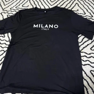 Svart Milano Italy t-shirt - Svart t-shirt med vit text 'MILANO ITALY' på bröstet. Klassisk rund halsringning och korta ärmar. Skön och enkel stil som passar till det mesta. Tillverkad i mjukt material för en bekväm känsla hela dagen.