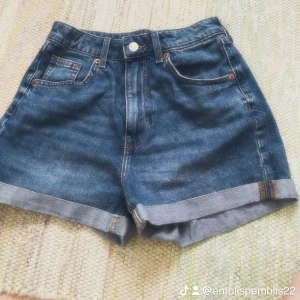 Blå jeansshorts från H&M Divided - Klassiska blå jeansshorts från H&M Divided i storlek 34. Modellen har upprullade benslut, fem fickor och bälteshällor. Snygg tvättad denim med normal passform, perfekta för varma dagar. Stängs med knapp och dragkedja framtill.