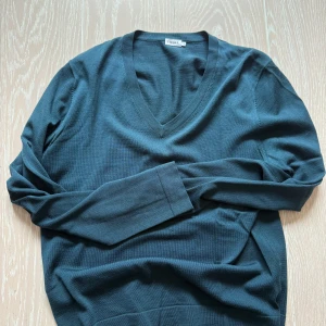 Mörkgrön v-ringad tröja från Filippa K - Snygg mörkgrön tröja från Filippa K med v-ringning. Perfekt för en stilren look. Tröjan har långa ärmar och är tillverkad i ett mjukt material som ger en skön känsla.