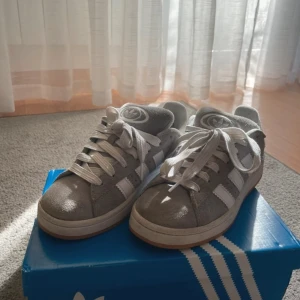 Grå Adidas Campus sneakers - Snygga grå Adidas Campus sneakers med vita ränder och snörning. Skorna har en klassisk design med en bekväm sula och är perfekta för en avslappnad stil. Kartong följer med!