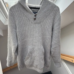 Grå Stickad hoodie - Säljer en grå stickad hoofie med knappar vid kragen och ett snyggt mönster. Perfekt nu till tidiga våren! Passar bra till de mesta, hör av er vid frågor🙌