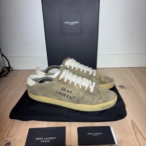 Saint Laurent skor size 43 passar 44 - Snygga beige sneakers från Saint Laurent med vit snörning och texten 'Saint Laurent' på sidan. Skorna har en klassisk design med en bekväm sula och är perfekta för en stilren look. Finns mer bilder bara höra av er priset går att diskutera vid snabb affär.