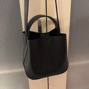 Svart axelväska från Gina - Snygg svart axelväska i syntetmaterial från Gina. Väskan har både handtag och en längre axelrem för flexibel användning. 150kr (Pris kan diskuteras) 💞Helt ny, aldrig använd