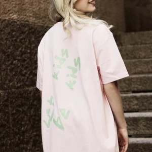 Rosa t-shirt med tryck från Gul & blå, stl xxs. Helt ny!!  - Säljer en helt ny T-shirt från Alicia Otteruds kollektion ihop med Gul & blå. En rosa t-shirt med grönt tryck 'Let kids be kids' på ryggen. T-shirten har en normal passform.   ”Let Kids Be Kids” handlar om att barn och vi tonåringar ska ha rätt till en barndom utan grooming och sexuella trakasserier!  Materialet är 100% ekologisk ringspunnen bomull. Ringspunnen bomull innebär att fibrerna går i samma riktning och blir på så sätt tåligare och mjukare. Fantastisk kvalitet! 