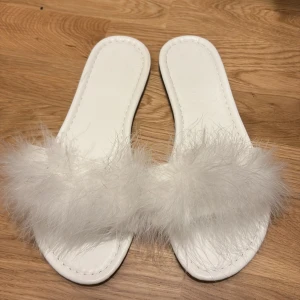 Vita sandaler med fluffig detalj - Snygga vita sandaler med en fluffig detalj över foten. Perfekta för att ge en lyxig känsla till din outfit. De har en enkel och stilren design med en mjuk sula för extra komfort.
