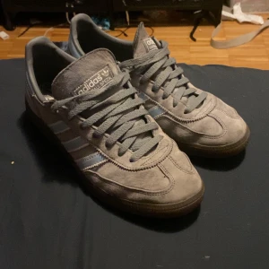 Grå Adidas Spezial med ljusblå detaljer - Snygga grå sneakers från Adidas med ljusblå ränder och detaljer. Skorna har en klassisk design med snörning och en robust sula. Perfekta för en avslappnad stil.