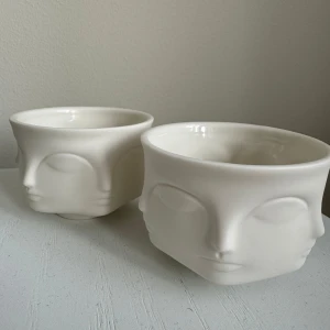 Vita ljuslyktor med ansiktsmotiv från Jonathan Adler - Säljer två vita ljuslyktor från Jonathan Adler med ett unikt ansiktsmotiv. Lyktorna är handgjorda i Kina och har en elegant design som passar perfekt för servering eller dekoration. Perfekt för att ge ditt hem en konstnärlig touch. Kan även användas som skålar. Aldrig använt, köpta för ca 500kr/styck !