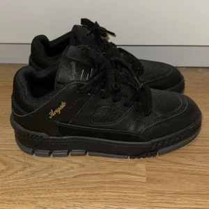 Svarta sneakers från Axel Arigato - Snygga svarta sneakers från Axel Arigato med guldfärgad logga på sidan. Änvänt ca 2 gånger så nästan helt nya.