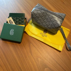 Grå necessär och grön korthållare  - Säljer en stilren grå necessär och en elegant grön korthållare. Necessären har ett klassiskt mönster och dragkedja, perfekt för att hålla ordning på dina saker. Korthållaren är kompakt och smidig.