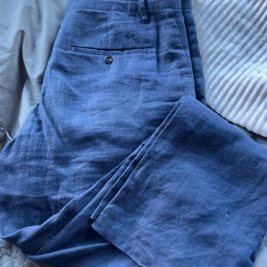 Blå linnebyxor från Gant - Snygga blå linnebyxor från Gant i en relaxed passform. Byxorna har en klassisk design med knappar och en bekväm midwaist. Perfekta för en stilren look.