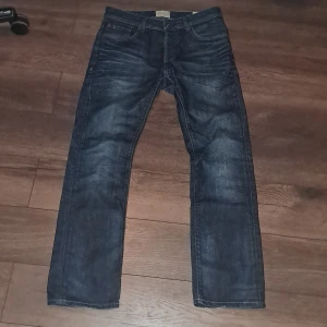 Mörkblå jeans från Jack & Jones - Snygga mörkblå jeans från Jack & Jones med klassisk femficksdesign. De har en straight passform och är perfekta för en avslappnad stil. Jeansen har en knappgylf och är tillverkade i slitstarkt denim.
