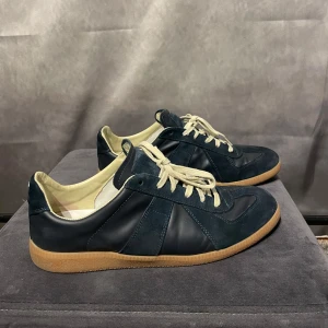 Maison margiela gats  - Snygga mörkblå sneakers med ovandel i mocka och skinn. Skorna har ljusbruna gummisulor och vita snören. Perfekta för en stilren look. Inget og tillkommer 