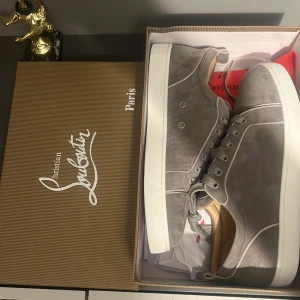 Grå sneakers från Christian Louboutin - Snygga grå sneakers från Christian Louboutin med den ikoniska röda sulan. Skorna har snörning och en stilren design som passar perfekt för en trendig look. Inte använd. 