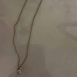 Guldhalsband med hänge - Elegant guldhalsband med ett litet hänge. Kedjan är tunn och smidig, perfekt för att bära till olika tillfällen. Hänget har en subtil design som ger en stilren look. Jag fick den i studentpresent så har aldrig använt det då det inte riktigt var min stil. (Tog studenten förra året)