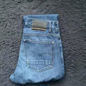 G-star jeans  - Snygga blå G star jeansbyxor med klassisk design. De har en rak passform och är perfekta för en avslappnad stil. Byxorna har fem fickor och en knappgylf. Perfekt för dig som gillar en tidlös look.