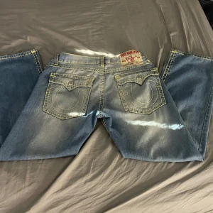 Blå jeans från True Religion - Säljer ett par baggy blå jeans från True Religion med klassiska bakfickor och kontrastsömmar. Tillverkade i USA. Stl w40 dom är insydda i midjan men d är lätt att sprätta upp om det behövs, kom privat för men info. Pris går att diskutera 