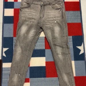 Gråa jeans från NVLTY - Snygga grå jeans från NVLTY med en sliten look och vita färgstänk. Byxorna har en klassisk femficksdesign och är använda sparsamt. Om du har frågor angående jeansen skicka bara ett meddelande✅