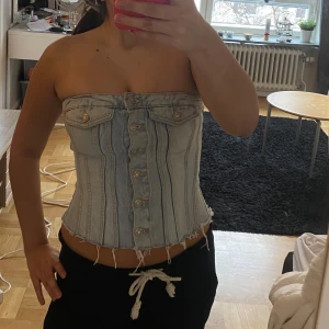 Ljusblå Jeans tubtopp med knappar - Säljer en snygg jeans tubtopp med knappar framtill. Toppen har en cool och trendig look med fransiga kanter och en figurnära passform. Perfekt för att styla med olika outfits!💕