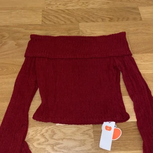 Vinröd offshoulder topp - Säljer en snygg vinröd offshoulder topp med långa ärmar. Toppen är ribbad och har en elegant design som passar perfekt för höst och vinter. Säljer pga den var för liten. Är märkt med s men passar snarare för xs