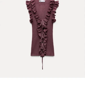 SÖKERR!!!Vinröd ribbad topp från Zara kan betala 300kr - Snygg vinröd ribbad topp från Zara med volangdetaljer längs v-ringningen. Toppen är ärmlös och har en knytning framtill som ger en extra touch. Perfekt för att lyfta din outfit med stil.