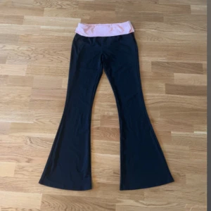 Svarta bootcut byxor med rosa midja! - Snygga svarta bootcut byxor med bred, mjuk och ljusrosa midja. Byxorna har utsvängda ben och är tillverkade i ett stretchigt material som känns skönt mot huden. Perfekta för dig som gillar en bekväm look.