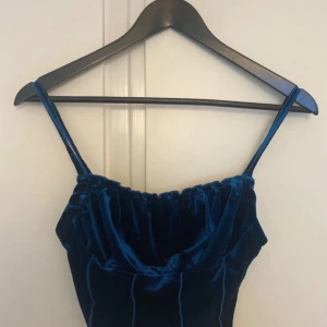 Blå sammetslinnetopp från SHEIN - Supersnygg blå linnetopp i sammetsmaterial från SHEIN. Toppen har smala axelband, croppad passform och coola vertikala sömmar som ger en trendig look. Perfekt att styla med jeans eller kjol för en extra pop av färg.