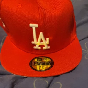 Röd LA Dodgers keps New Era 59FIFTY - Snygg röd LA Dodgers keps från New Era 59FIFTY-serien. Kepsen har broderad LA-logga framtill, 1988 World Series-märke på sidan och MLB-logga bak. Tillverkad i 100% polyester och har klassisk flat peak. Perfekt för dig som gillar sportig streetstyle.