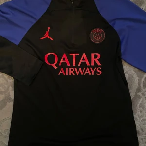 PSG set - Säljer ett fett PSG x Jordan träningsset med svart och blå tröja och matchande svarta byxor. Tröjan har röda loggor, halv dragkedja och blå ärmar. Byxorna har röda detaljer och PSG-märke. Perfekt för fotboll eller chill.