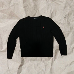 Svart stickad tröja från Polo Ralph Lauren - Säljer en klassisk svart stickad tröja från Polo Ralph Lauren. Den har en diskret röd logga på bröstet och är perfekt för både höst och vinter. Tröjan är i mycket bra skick och har långa ärmar. Perfekt för en bekväm stil. Tröjan är sparsamt använd och passar folk som är 170-180. 