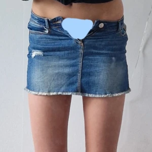 Blå jeanskjol från Zara  - Snygg blå jeanskjol från Zara med slitna detaljer och fransad nederkant. Klassisk femficksmodell med knapp och dragkedja framtill. Perfekt för dig som gillar en cool och avslappnad stil.