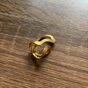 Guldig vågig statementring - Cool ring i guld med vågig, öppen design och tunna linjer som ger en modern och unik look. Perfekt för dig som vill sticka ut med ett smycke som verkligen syns. Passar både till enkla och mer kreativa outfits.