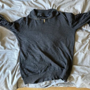 Mörkgrå half zip tröja Jack & Jones - Mörkgrå långärmad tröja från Jack & Jones med half zip-dragkedja i halsen. Tröjan har ribbade muddar och en klassisk, enkel design som funkar till det mesta. Materialet känns mjukt och bekvämt, perfekt för kyligare dagar.